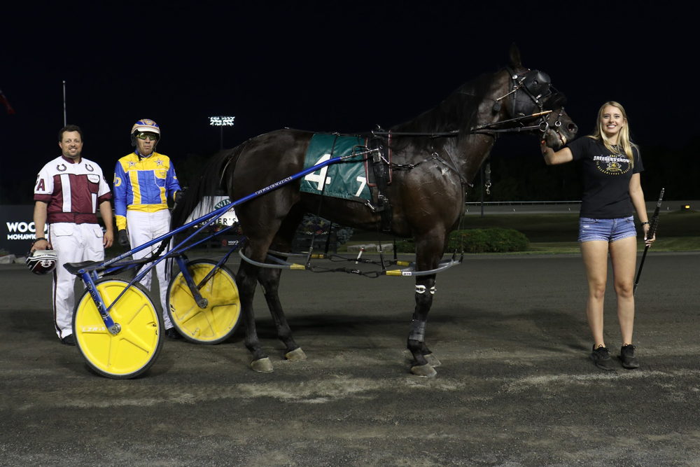 Carmen Auciello, driver Jonathan Drury, and Paige Austin with Outcast Blue Chip in the winner's circle on July 8, 2022 at Woodbine Mohawk Park (New Image Media)