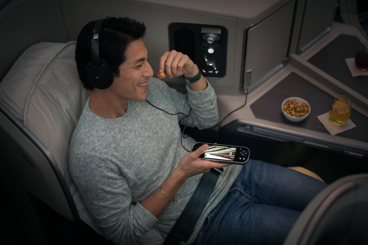 a man sitting in an airplane eating cereal and holding a phone