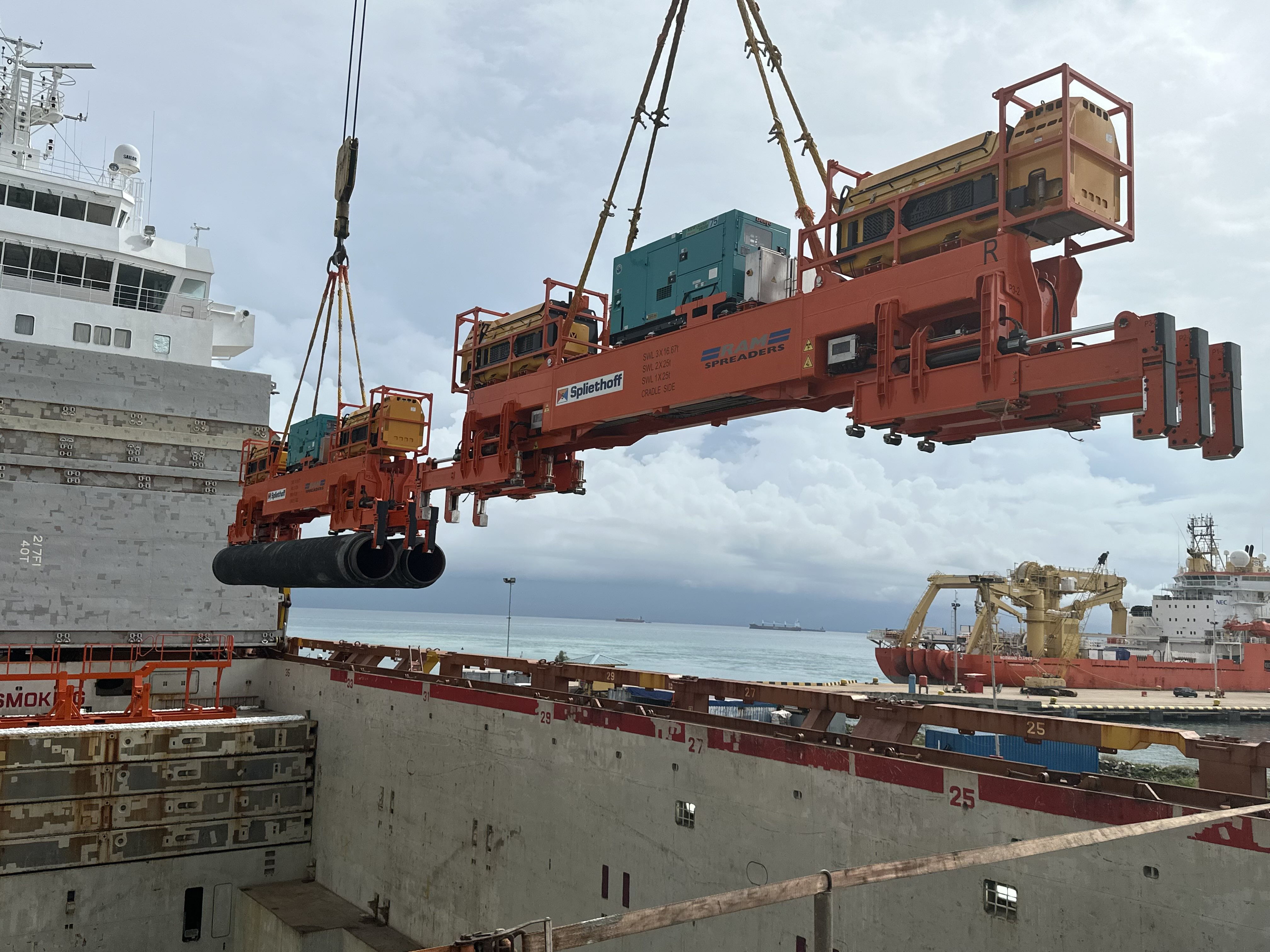 Two yellow Verton SpinPods control the rotation of each pipe-spreader while loading pipeline-sections into the hold of a Spliethoff vessel.