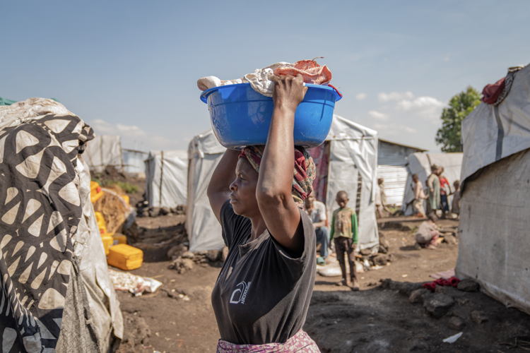 Esther, 41, carries supplies in Elohim camp near Goma. For a year and a half, she has lived here with her mother-in-law, daughters, and their children after fleeing the fighting in North Kivu. Copyright: Moses Sawasawa