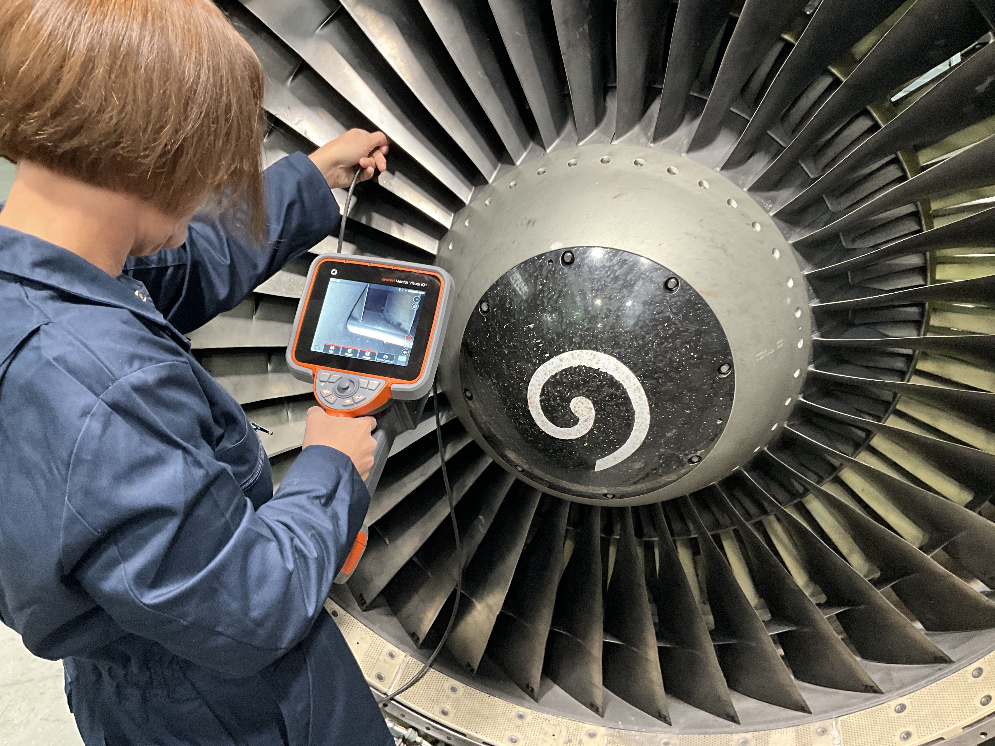 An operator using a Mentor Visual iQ+ video borescope to inspect a GE engine