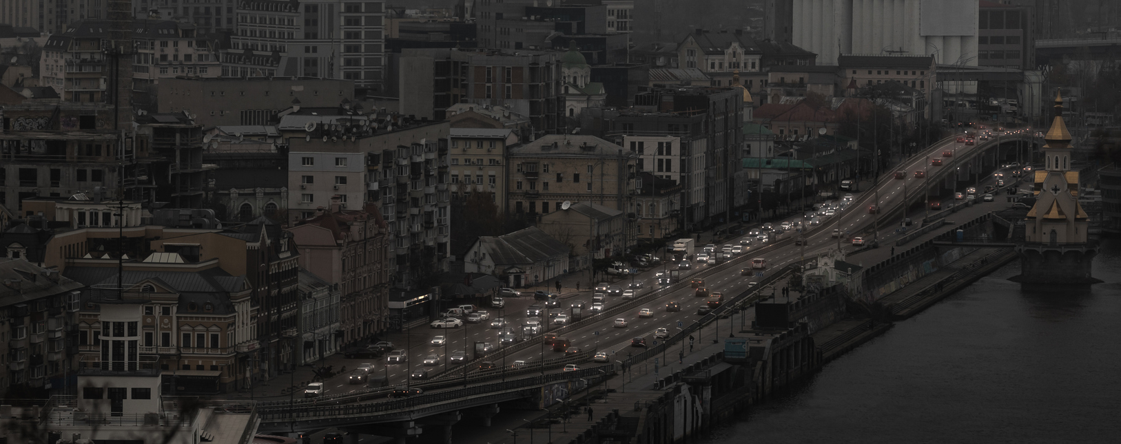 View of Kyiv from the observation deck in the evening during a blackout. Dark houses and unlit streets are visible, with only the lights of passing cars visible.