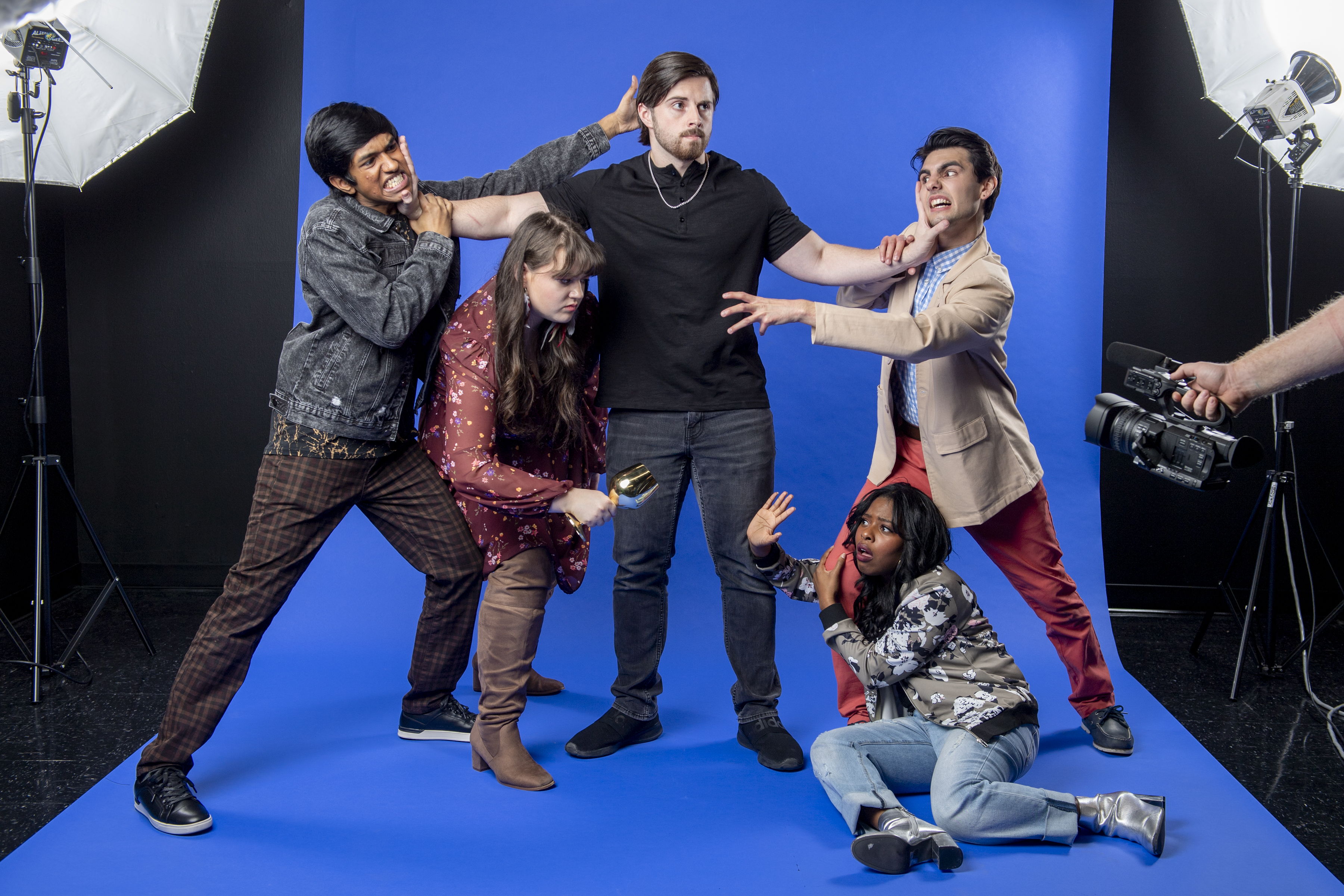 Cast members of "A Midsummer Night’s Dream" pose before a blue screen with lighting and camera equipment, showcasing the modern twist on Shakespeare’s classic play.