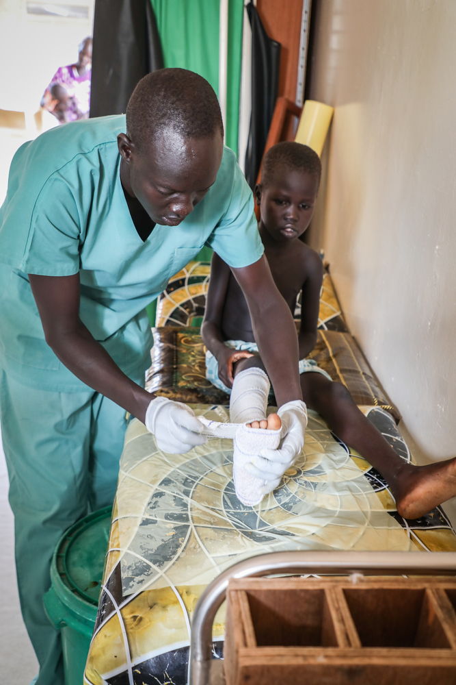 Un enfermero de MSF cambia el vendaje de Aluk Manut, de 6 años. Aluk mordida por una serpiente en la pierna derecha. Aluk y su madre, Teresa Aluoc Majok, tuvieron que desplazarse 150 km para llegar al hospital en Agok, Sudán del Sur. Aluk recibió tres dosis de antídoto y ha tenido siete operaciones quirúrgicas. © Fanny Hostettler