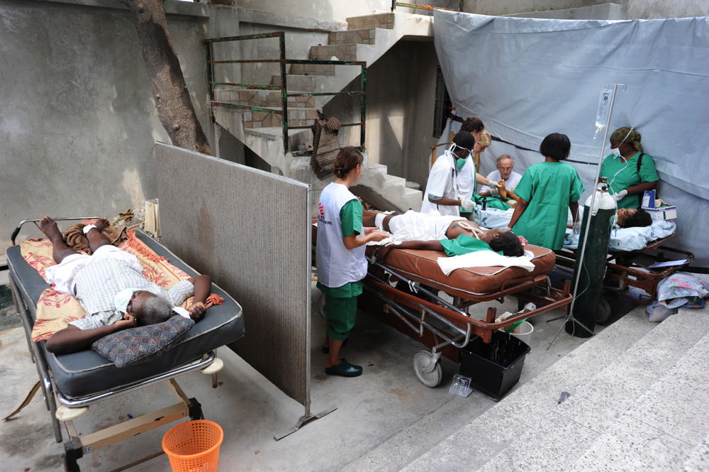 MSF surgeon works on a patient with a broken foot in the makeshift surgery room of the Martissant hospital. It is under the shade of a tree outside the hospital. 17 Jan 2010. Copyright: Julie Remy