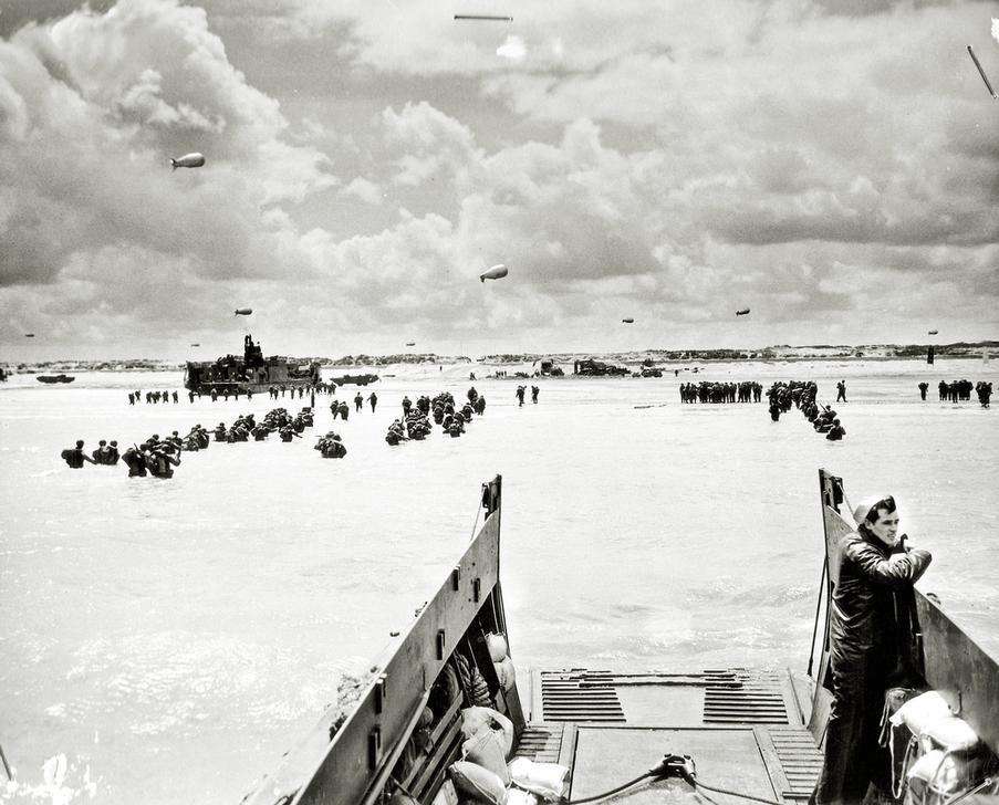 AKG2492530 Allied soldiers are walking in deep water during the invasion of the beach. On the left is the Landing Craft, Tank (LCT) –779. Barrage balloons are in the sky. In the foreground is a Landing Craft, Vehicle, Personnel (LCVP), which has landed reinforcements. Utah Beach, Normandy, France. ©akg-images