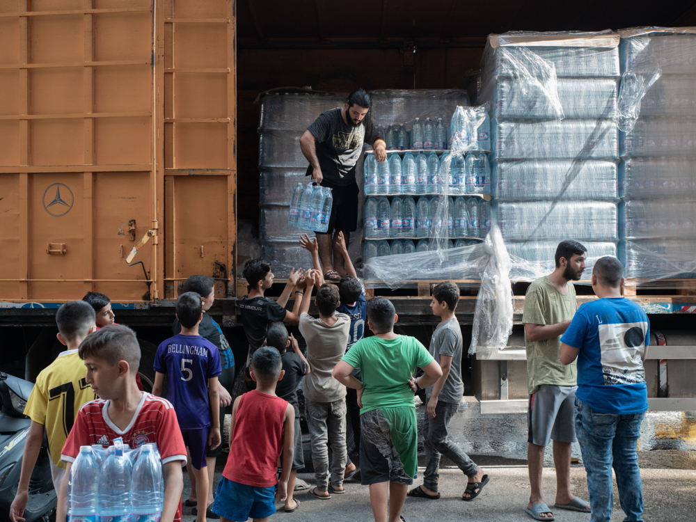 Kinderen van ontheemde gezinnen verzamelen flessen water tijdens een waterdistributie in het Azariehshelter in het centrum van Beiroet. (c) Antoni Lallican/Hans Lucas