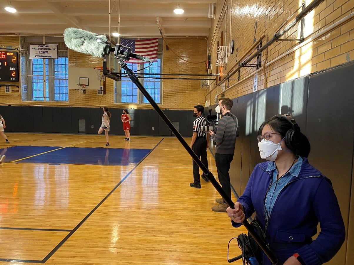 Steph Ching uses the MKE 600 with the MZH 600 Windshield, and HD 280 PRO monitoring headphones to capture audio in a gymnasium during the making of Slumlord Millionaire.