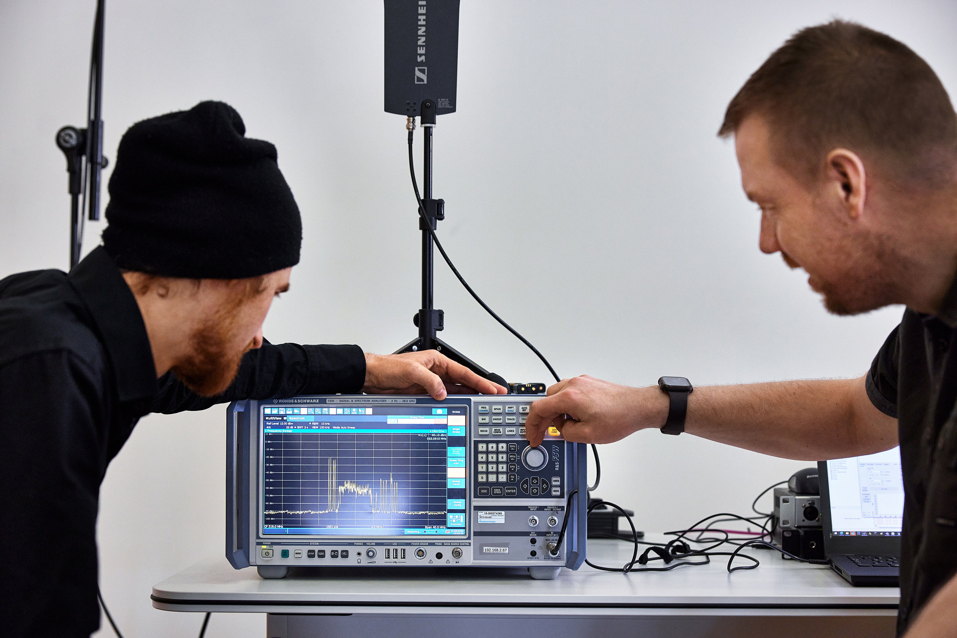 Marco Völzke (l.) und Jonas Naesby am Spektrumanalysator. Das Gerät zeigt links vom Breitbandsignal des WMAS-Systems vier IEM-Träger mit hoher Sendeleistung und rechts davon acht schmalbandige EW-DX-Träger