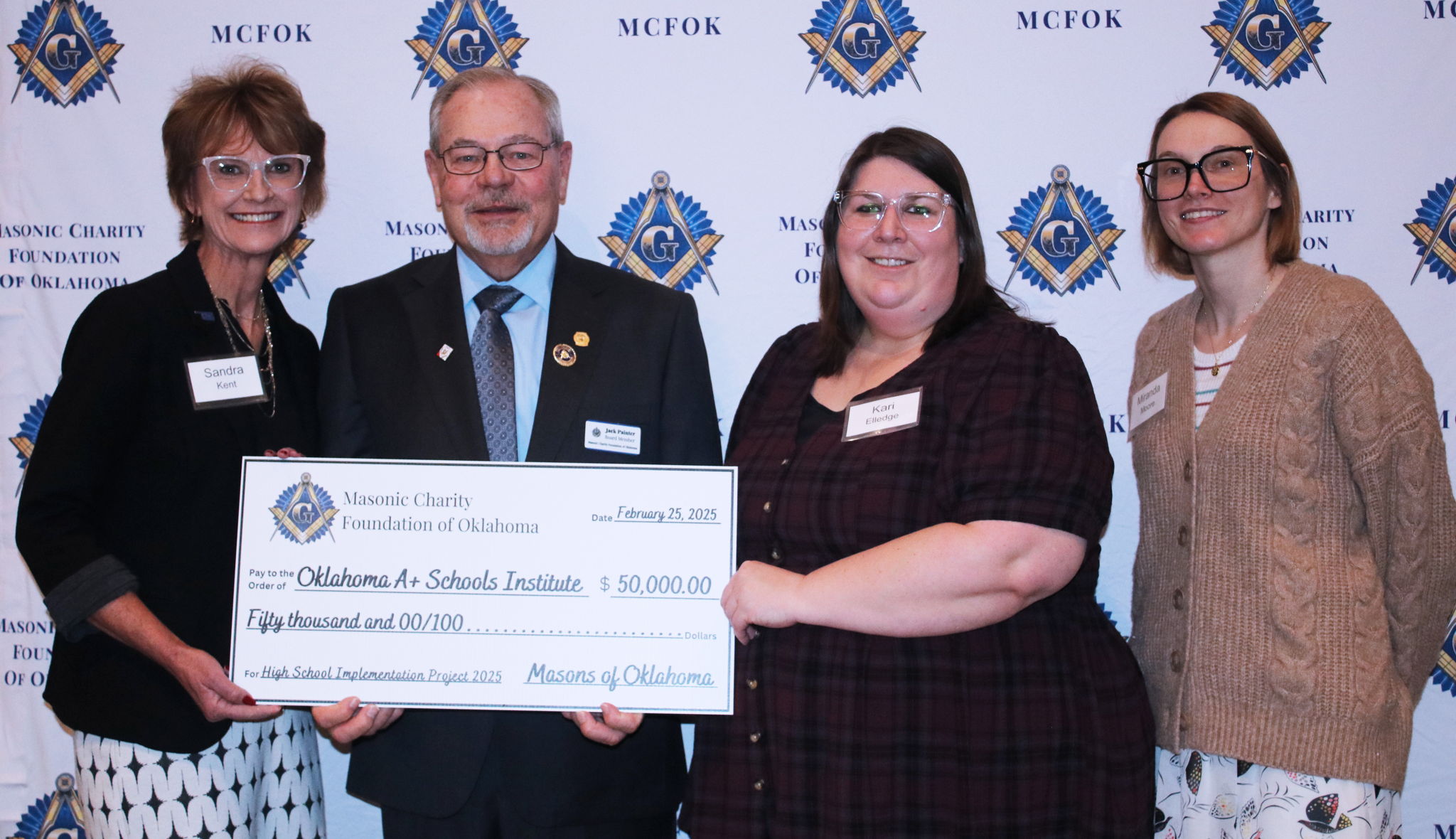 Four people pose while holding a large check for $50,000. Four people pose while holding a large check for $50,000.