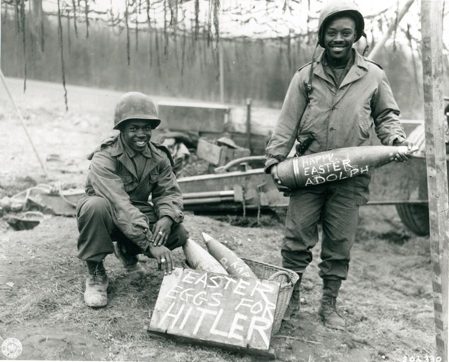 AKG821031 US soldiers, T–5 William E. Thomas and PFC. Joseph Jackson, present a basket of artillery shells, labelled “Easter Eggs for Hitler” ©akg-images