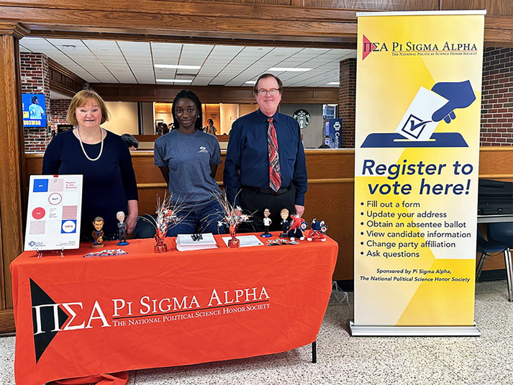 Three individuals stand behind a table as they host a voter registration event