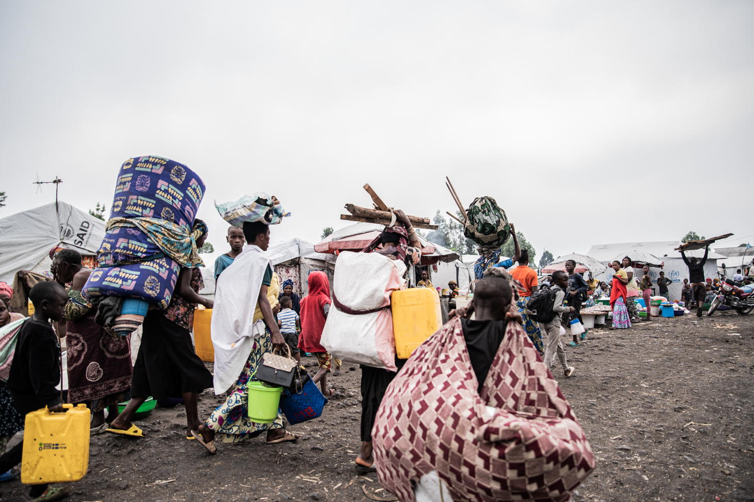 Title: IDPs leaving Goma camps. Copyright: Jospin Mwisha Countries: Democratic Republic of Congo Date taken / Date Recorded: 11 February, 2025 Caption / Description: Des familles quittent les camps de Lushagala et Bulengo, portant leurs colis sur le dos et sur la tête. Certains déplacés prennent la route à pied, se disant que ce n’est pas loin et que c’est mieux que de mourir ici, dans le camp. Page 3