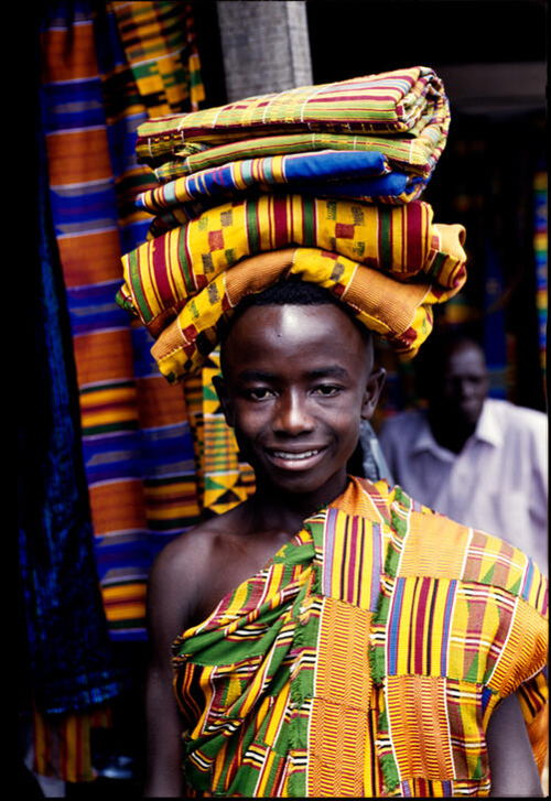 A young Ghanaian man balances a stack of Kente cloth on his head. AKG11123644 © akg-images / Margaret Courtney-Clarke / african.pictures