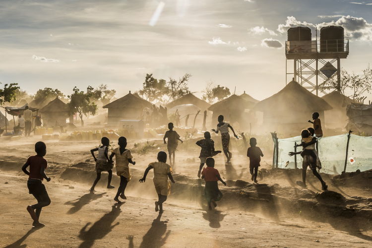 Kinderen spelen in Bidi Bidi kamp. Op de achtergrond een watertoren en tenten © Frederic Noy
