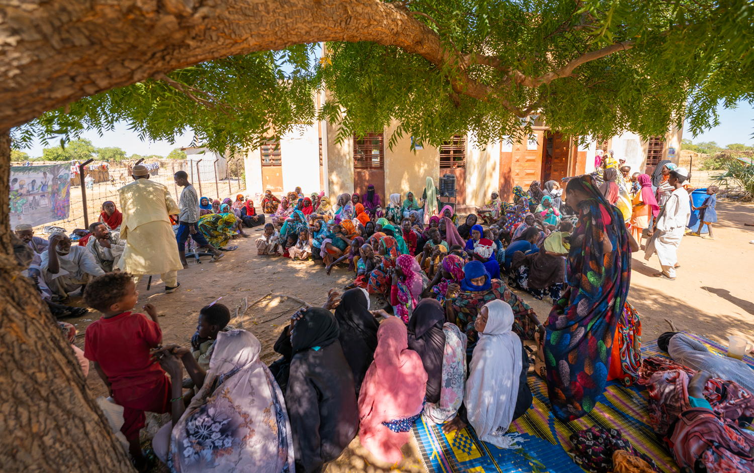 Een menigte repatrianten en vluchtelingen wacht in de rij onder een boom op zorg van het mobiele kliniekteam van AZG in de informele nederzetting Jerbana.© Isaac Buay/MSF