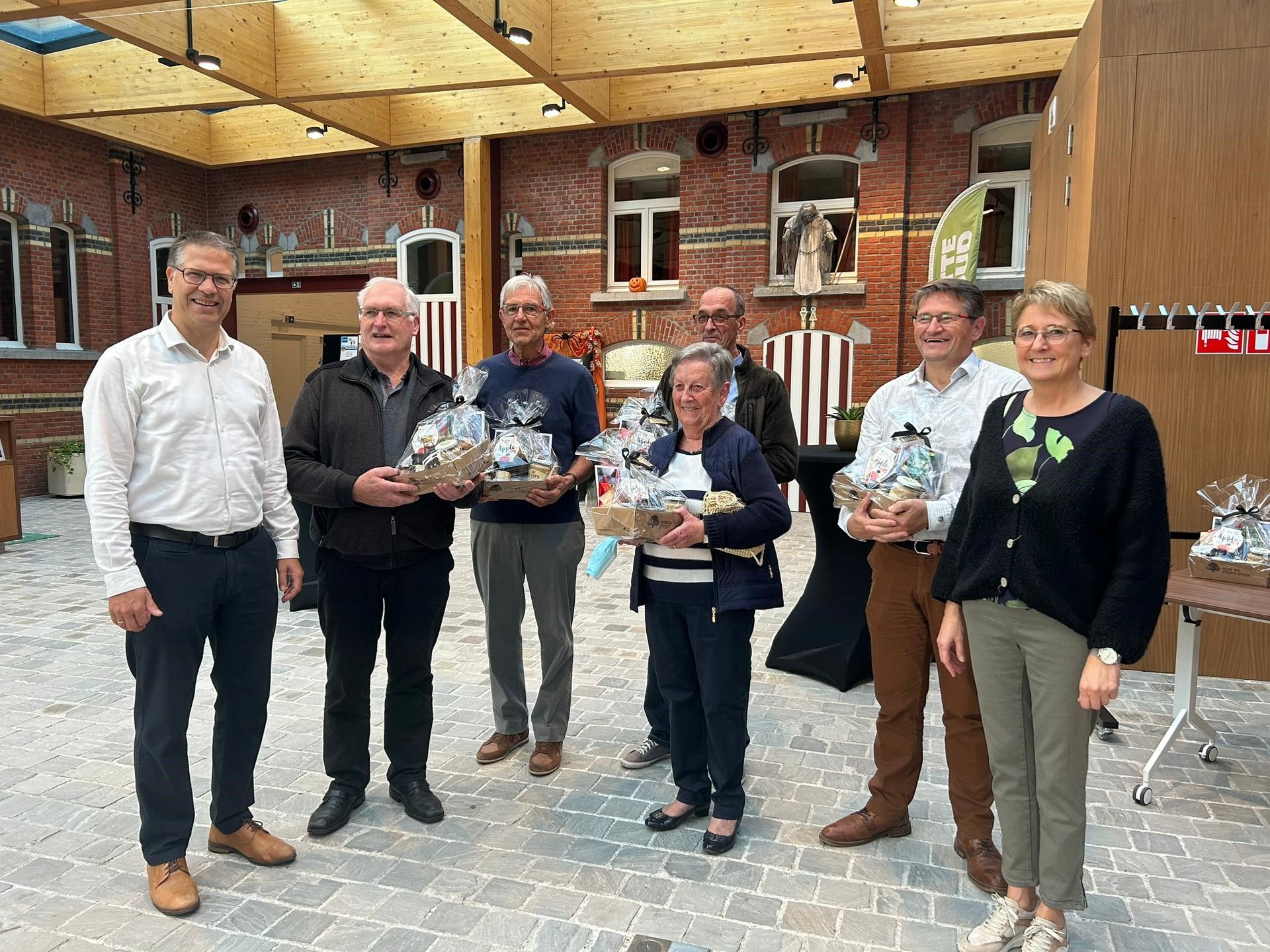 Gedeputeerde Tom Dehaene en schepen Greet Willems schenken een streekproductenpakket aan de 8 vrijwilligers bij de start van de Minder Mobielen Centrale in Kampenhout