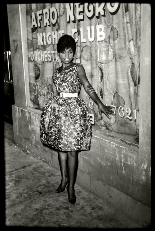 Jean Depara, A beautiful Kinshasa woman belted in her tulip dress in front of the Afro Negro Club, City-Five orchestra, 1960 © Estate DEPARA, courtesy of Magnin-A Gallery 