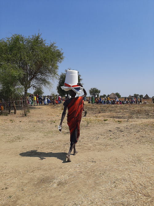 A mother walks back home carrying a kit donated by MSF in Riang, Jonglei State. It contains mosquito nets, blankets, buckets, soap, water purifiers and filters, a plastic sheet and rope.  Copyright: Damaris Giuliana/MSF