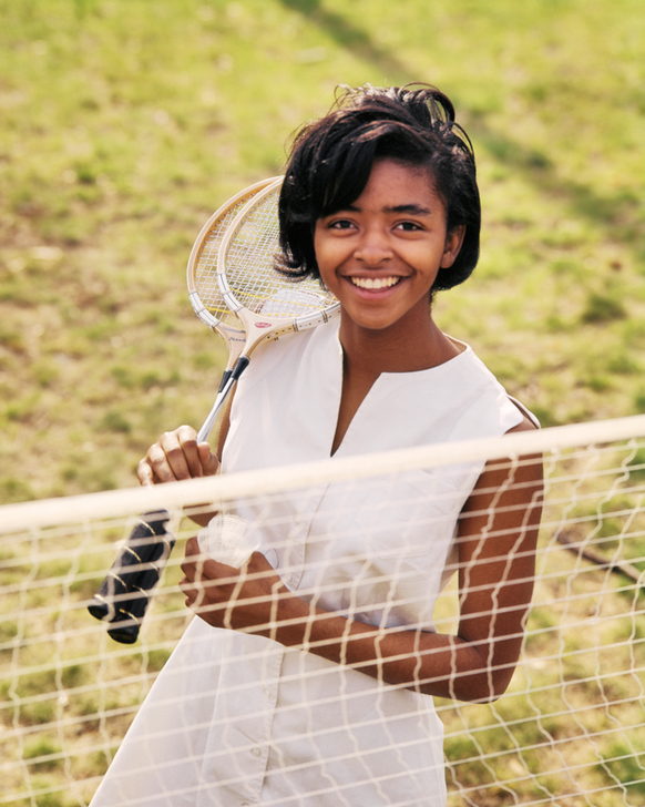 AKG7725398 1960s TEENAGE GIRL WHITE SPORTS OUTFIT SMILING OVER TOP BADMINTON NET LOOKING AT CAMERA HOLDING TWO RACQUETS. © akg-images / ClassicStock