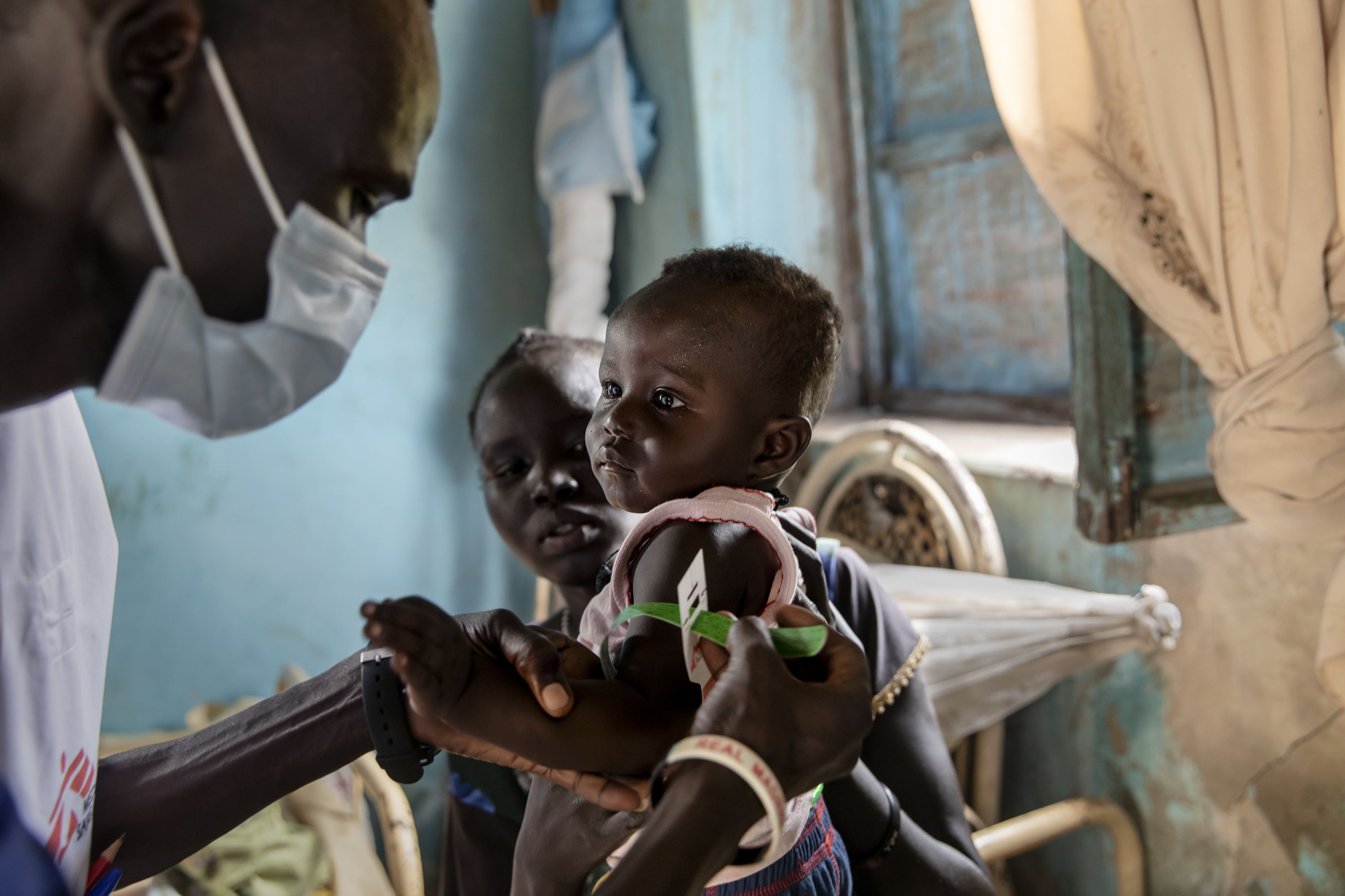 Ajok Atak, sostiene a su hijo Yel mientras un miembro del personal de MSF mide el nivel de nutrición del niño en su casa cerca de Kuom, Sudán del Sur. © Adrienne Surprenant