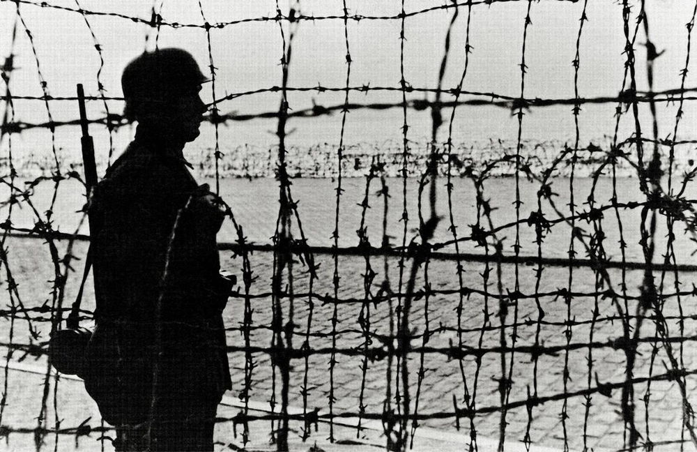 A German soldier is on guard duty behind barbed wire defences on the coast in Normandy, France. AKG2492457 © akg-images