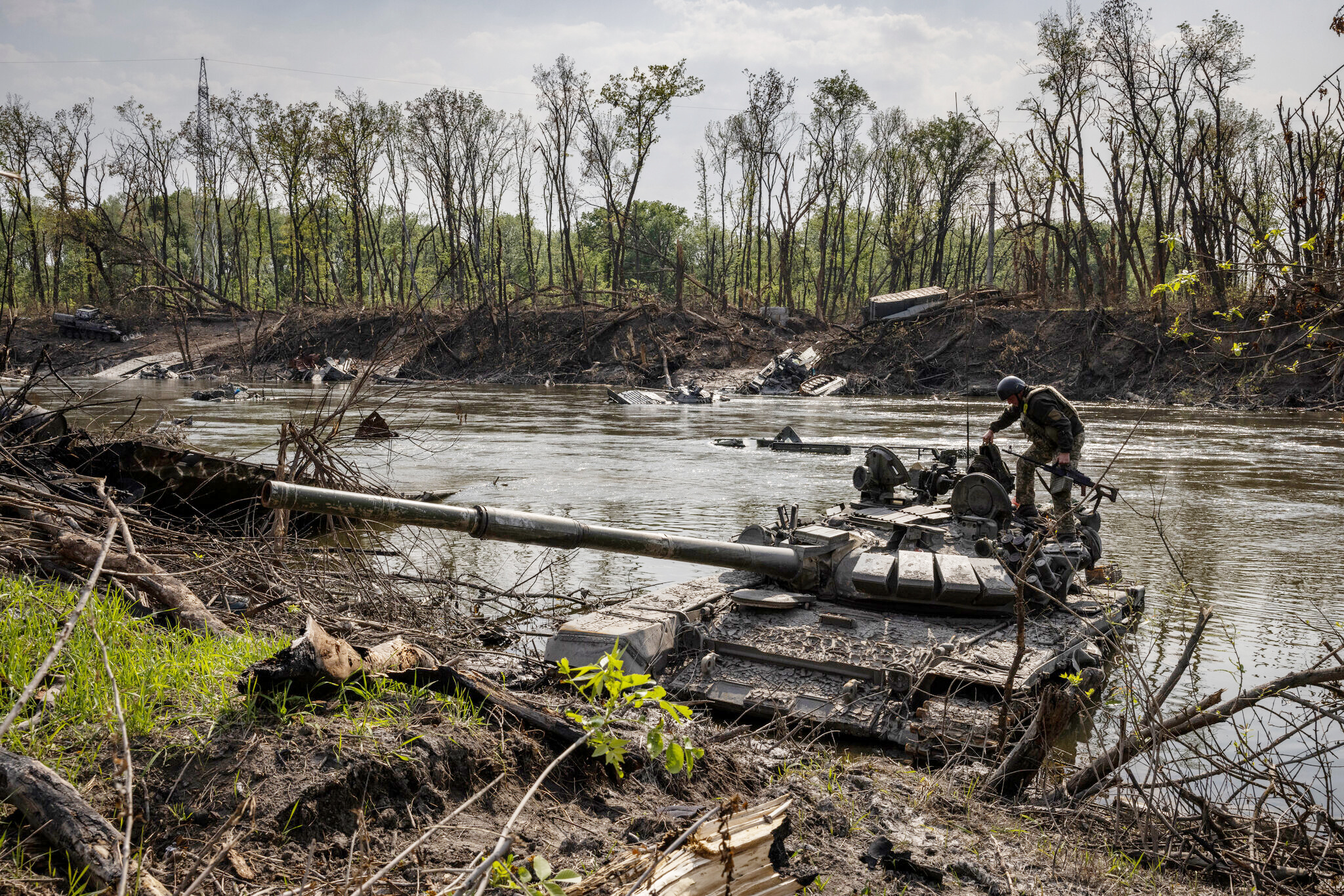 A Ukrainian soldier atop an abandoned Russian tank in the Seversky Donets river in order to salvage a heavy machine gun left behind. Image courtesy of The New York Times 