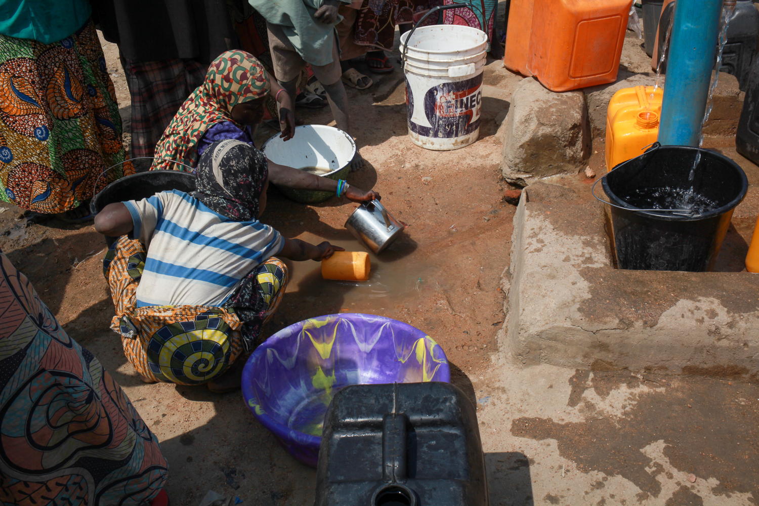  Children scoop up spilled water from the ground by a borehole in Pulka. Some people use this spilled water to wash themselves and their clothes, as there isn´t always enough clean water to drink and cook with, let alone clean with. Photographer: Scott Hamilton