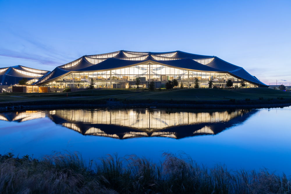 A photo of Bay View’s larger building at twilight reflects in the stormwater retention pond, part of the water-positive design of the campus. (Photo: Iwan Baan)