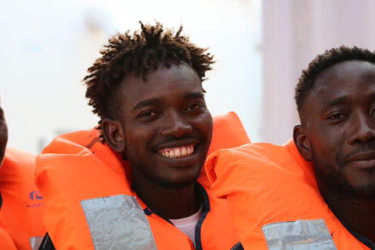 Rescued people smile as the MSF and SOS MEDITERRANEE prepare them to be transferred to the Armed Forces of Malta for disembarkation in Malta. Photographer Hannah Wallace Bowman Location Med Sea  24082019 (1)