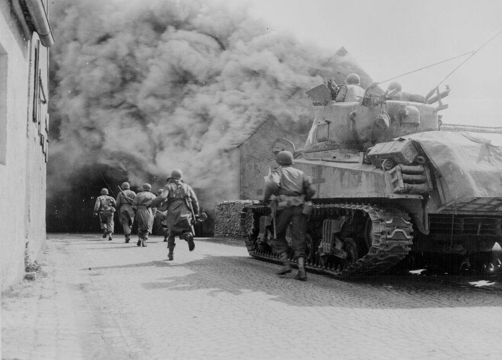 Soldiers of the 55th infantry batallion advance protectetd by a tank from the 22nd US tank division, Ardennes Offensive. AKG419950 © akg-images
