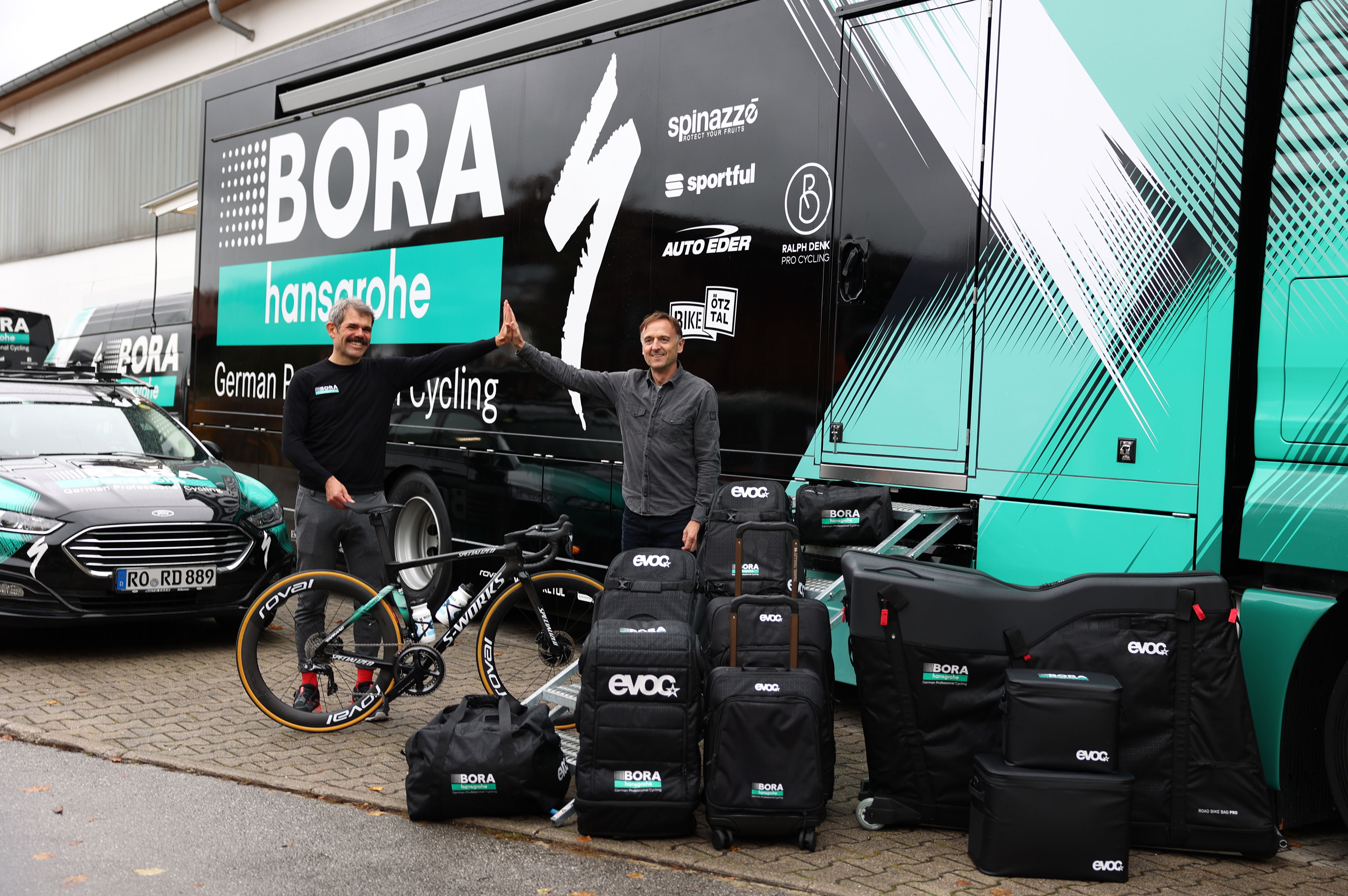 Teamchef Ralph Denk und EVOC Mitgründer Holger Feist (v.l.n.r.) bei der Übergabe der BORA – hansgrohe Kollektion von EVOC | ©EVOC – Marco Schmidt