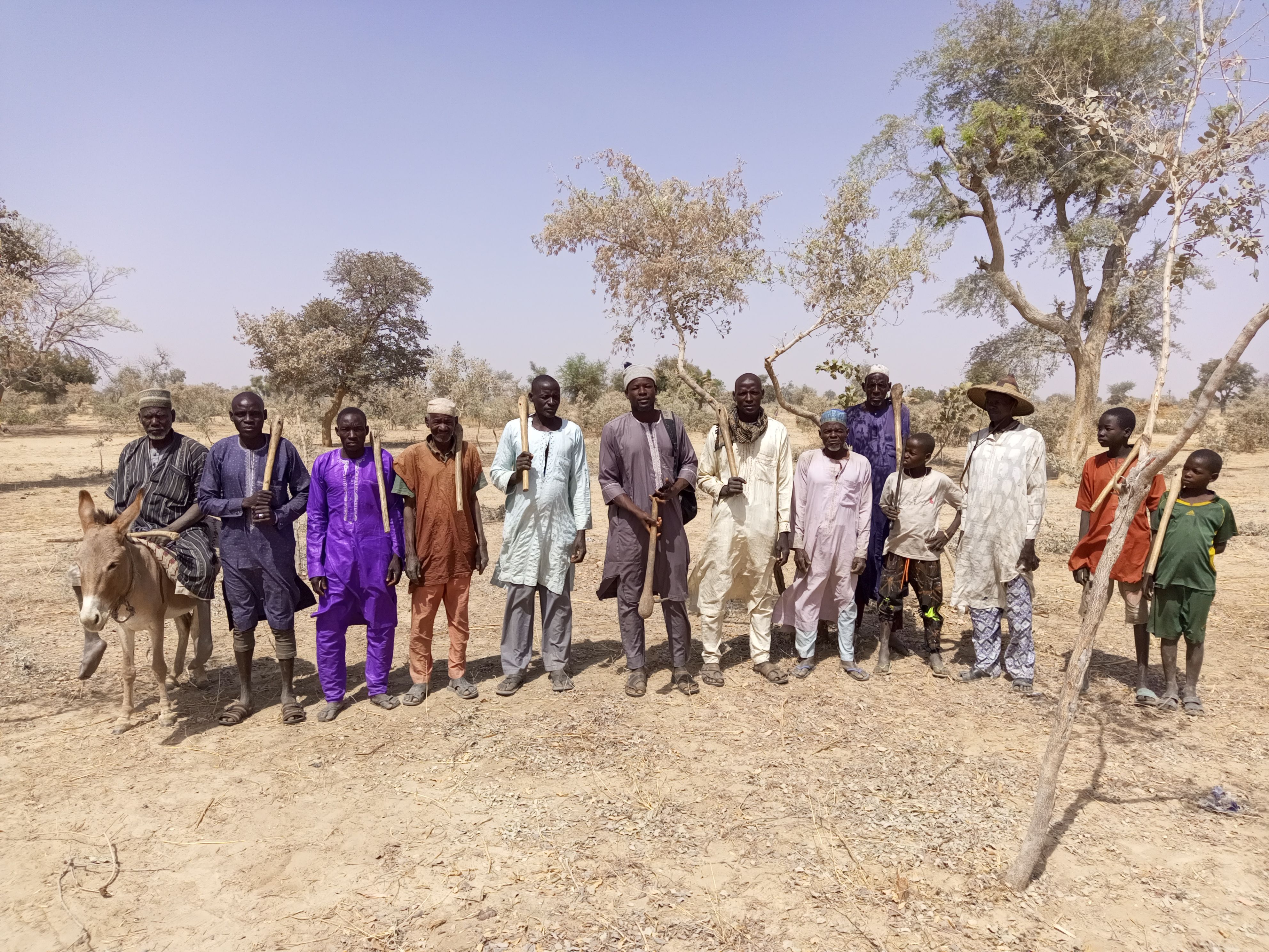 FMNR committee members from Bagari Village in Magaria Commune, Zinder Region, actively engaged in monitoring activities. The Village Chief, positioned on the left, and several young community members are present, underscoring their involvement and support in the FMNR process.