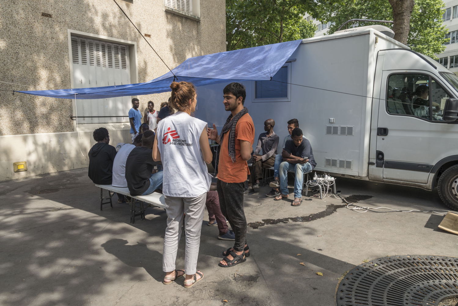 Vue de la clinique mobile. Pendant l'attente l'équipe MSF distribue de l'eau et des compotes face aux dernières grosses chaleurs. Ils discutent avec les migrants et les réfugiés afin de mieux catégoriser leurs problèmes de santé. © Rémy Decoster/MSF