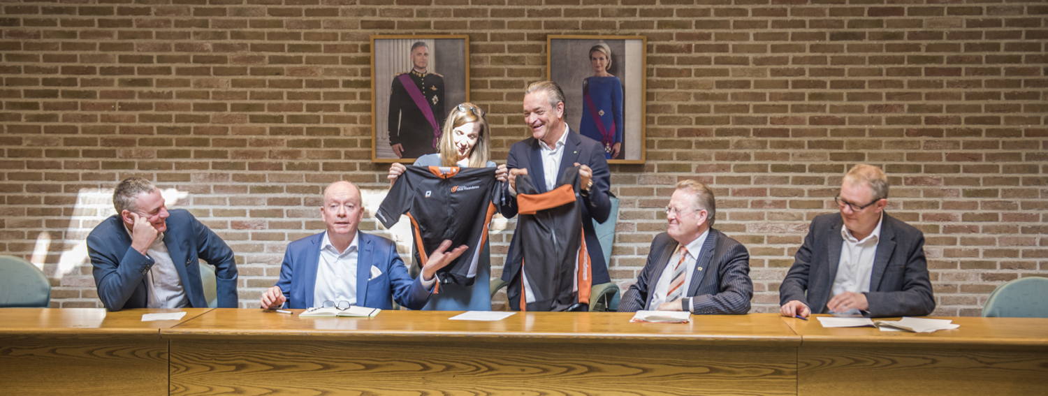 Gedeputeerde Hilde Bruggeman overhandigt een wieleroutfit aan de burgemeester van Herzele Johan Van Tittelboom