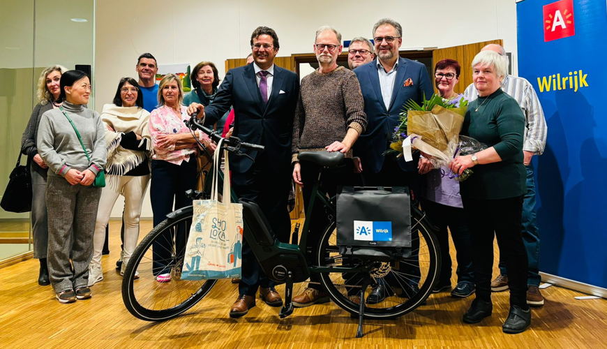 Winnaar Wim Vermeulen samen met districtsburgemeester Bossuyt, Antwerps schepen Kennis en een groep Wilrijkse handelaren die deelnamen aan 'Liever Lokaal'.