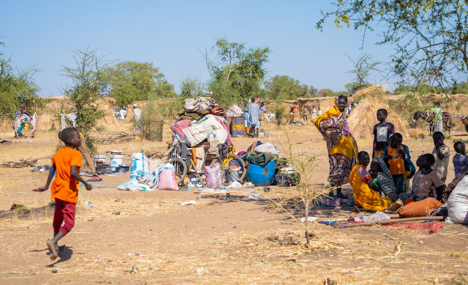 Een pas aangekomen gezin zit in de schaduw in de Jerbana nederzetting. Sinds hun aankomst drie dagen geleden slapen ze in de open lucht. © Isaac Buay/MSF
