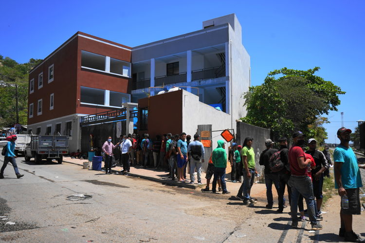 Dozens of migrants line up outside the shelter of the Casa del Migrante Diocesis of Coatzacoalcos to receive food. Due to the COVID-19 pandemic, the shelter authorities are not allowing access to migrants. Men, women and families with their children have to sleep under the bridge or next to the tracks.