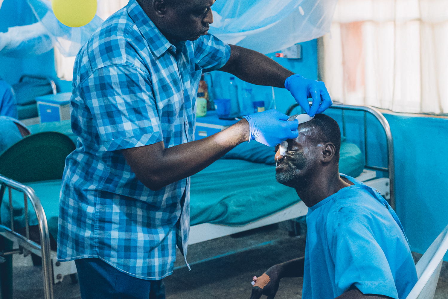 Dr Kefas Mbaya, plastic surgeon, changes the bandages of Amadu, a 45-year-old noma survivor from Bauchi state, in the postoperative ward of the Sokoto Noma Hospital. ‘They have genuinely embraced me, both men and women. I feel as though I am at home. They respect me,’ says Amadu about the people in the hospital. Photographer: Fabrice Caterini. Date: 08/05/2023 . Location: Nigeria 