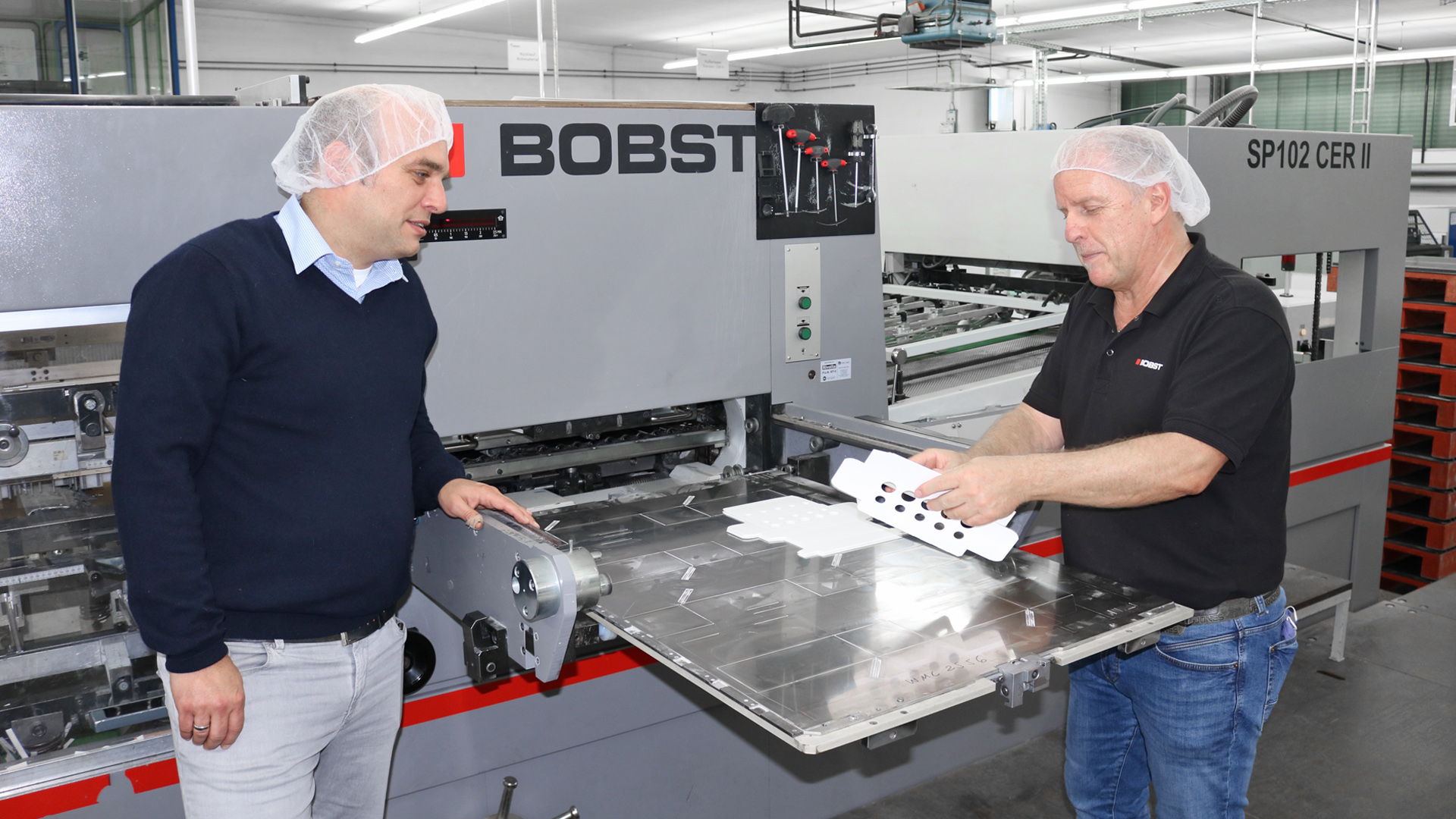董事总经理迈克尔·斯皮格尔（左）和博斯特梅尔布施的曼弗雷德·沃宁（右）站在博斯特SP102 CER II模切机旁.