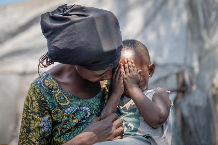 Tuliya smiles while holding her son Gadi in her arms in Elohim camp. They have lived here for a year and a half to escape the fighting in North Kivu. Copyright: Moses Sawasawa