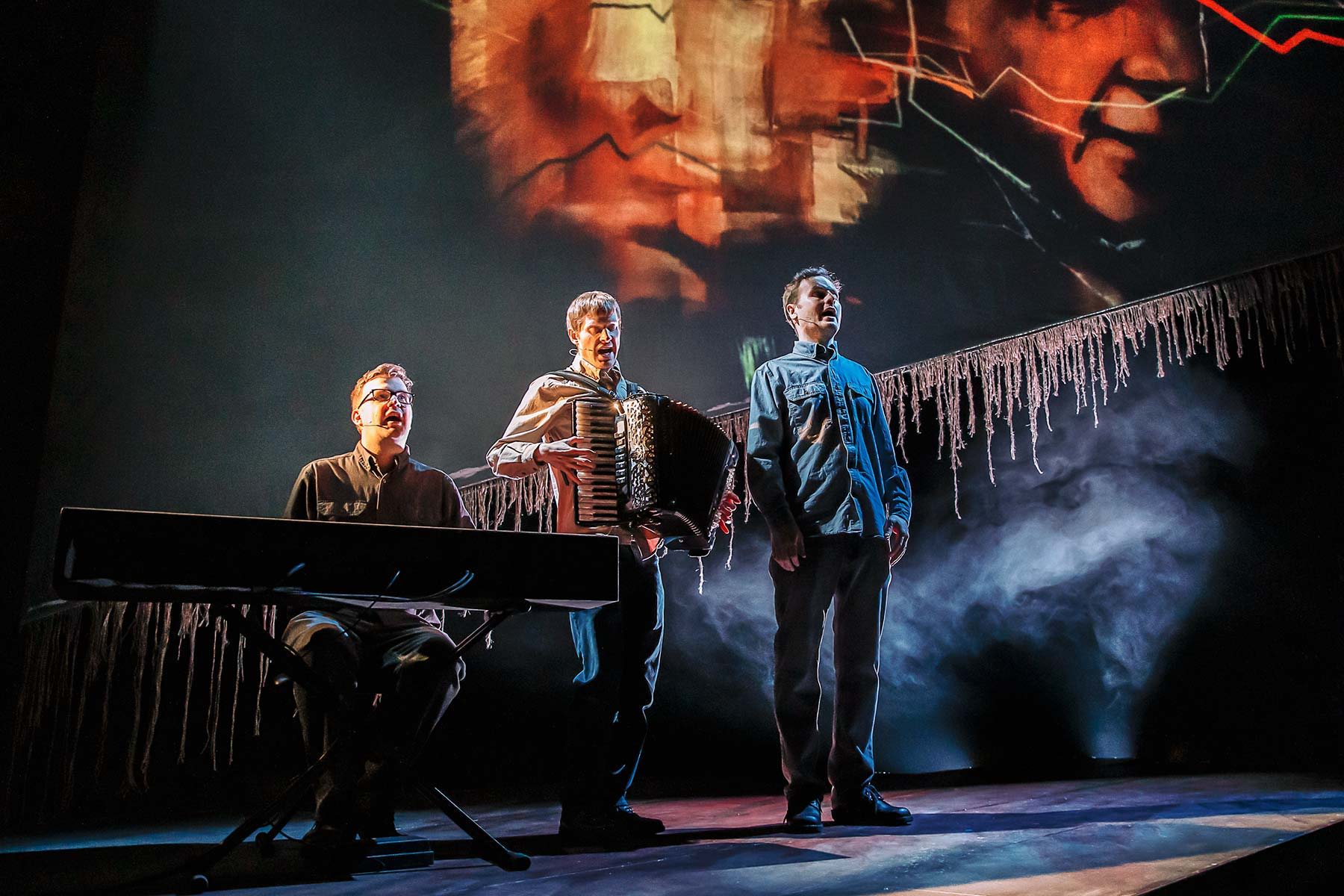 UK folk band The Young'uns onstage performing The Ballad of Johnny Longstaff in the spotlight on a dark-lit stage in London's West End.