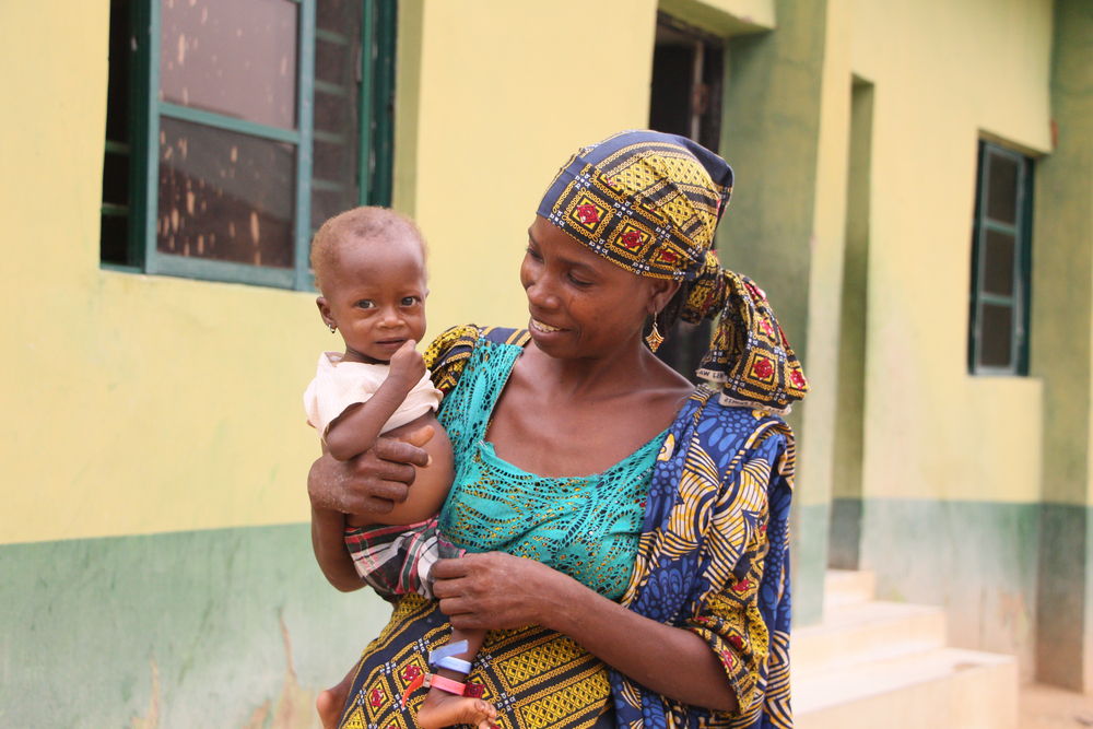 Hadiza Musa stands holding her daughter Ni’ima at the front of the Inpatient Therapeutic Feeding Center in Zurmi General Hospital, Zamfara state, Northwest Nigeria. Photographer: Abba Adamu Musa|Location: Nigeria |Date: 30/05/2024