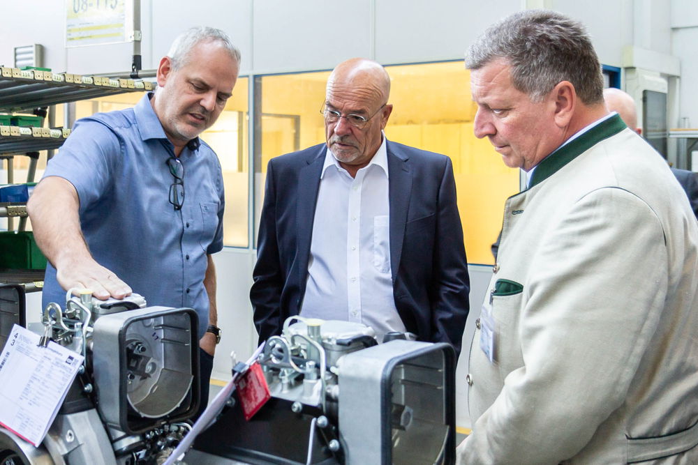 Christian Kasbauer (links), Leiter der Produktion Motoren und Systeme bei Hatz, gibt zusammen mit Wolfram Hatz (Mitte), Hauptgesellschafter und Beiratsvorsitzender bei Hatz, Staatsminister Christian Bernreiter einen tieferen Einblick in die Motorenmontage.