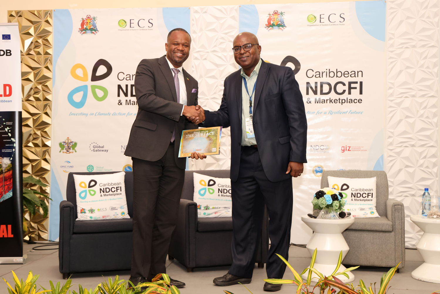 L'honorable Konris Maynard, président du Conseil des ministres de l'énergie (à gauche) accepte l'exemplaire de la brochure inaugurale du programme GEOBUILD de l'OECO intitulée « Power Below The Surface : The Power Below The Surface », de la part du Dr. Ernie Stapleton. Ernie Stapleton, chef de projet, OECS GEOBUILD, à l'issue du 3e forum et marché d'investissement sur les CDN qui s'est tenu au Radisson Grenada Beach Resort.