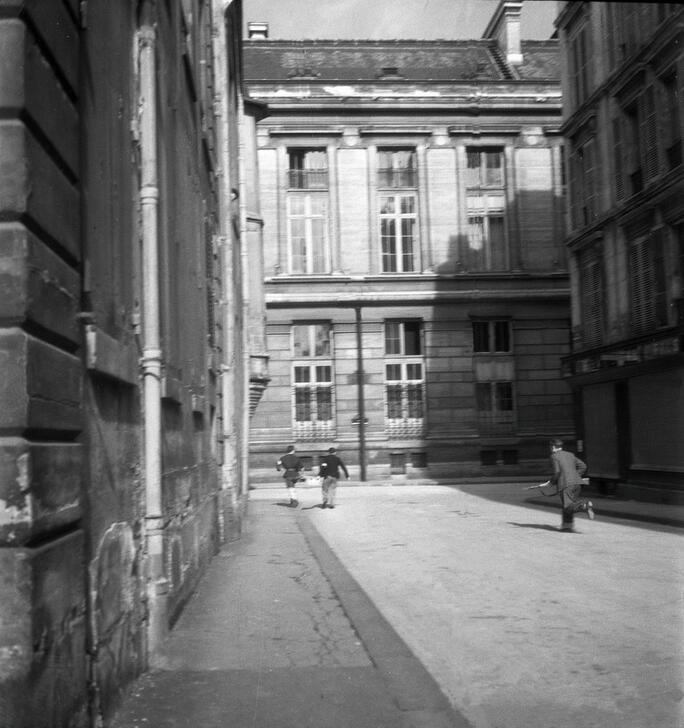 Two men carrying something together and another armed man run down the Rue Pierre Sarrazin, towards the Rue Hautefeuille. In the background, the east facade of the Museum of the History of Medicine. AKG10792617 © René Zuber / akg-images