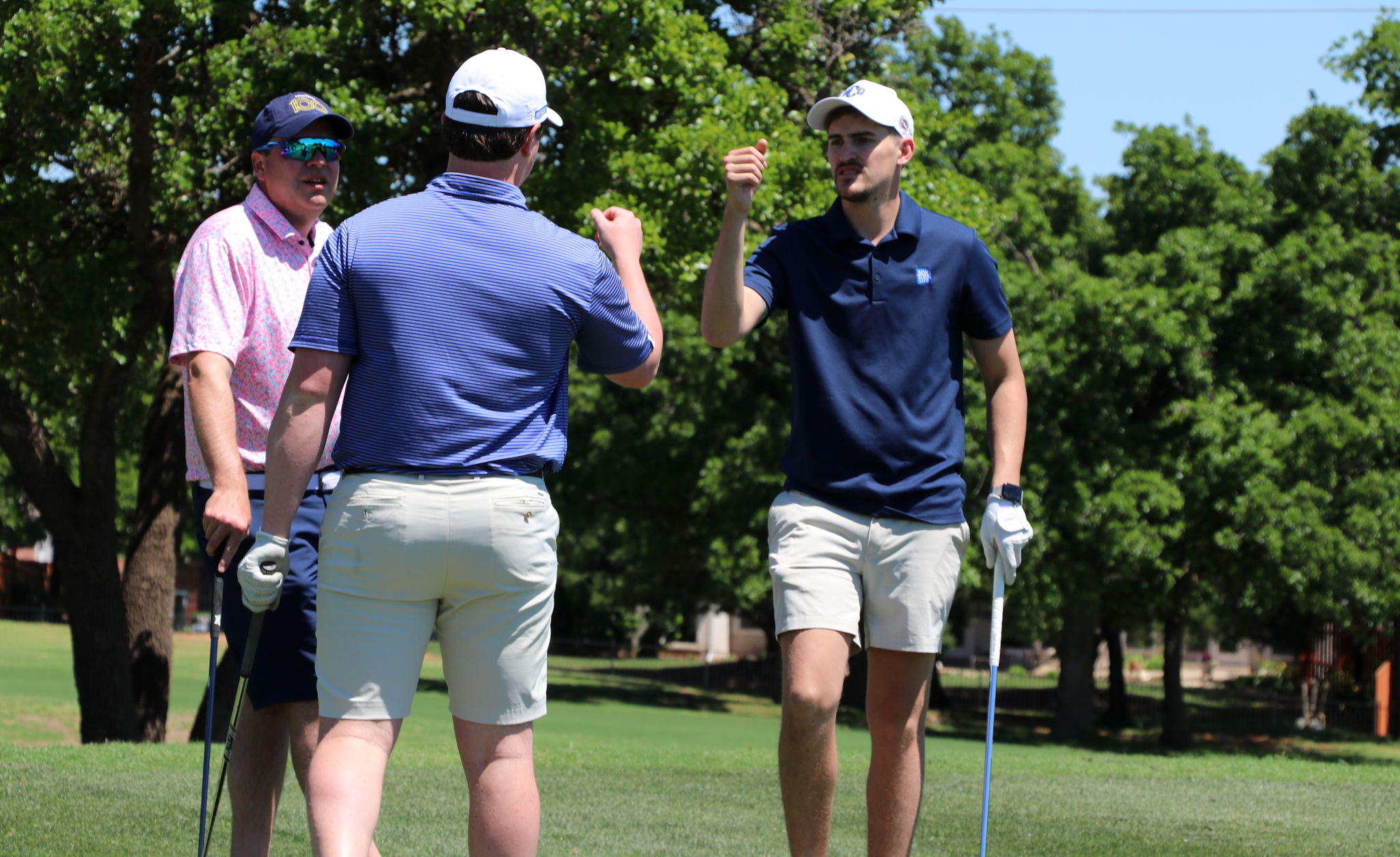 Two individuals golfing and giving each other a fist bump on the course.