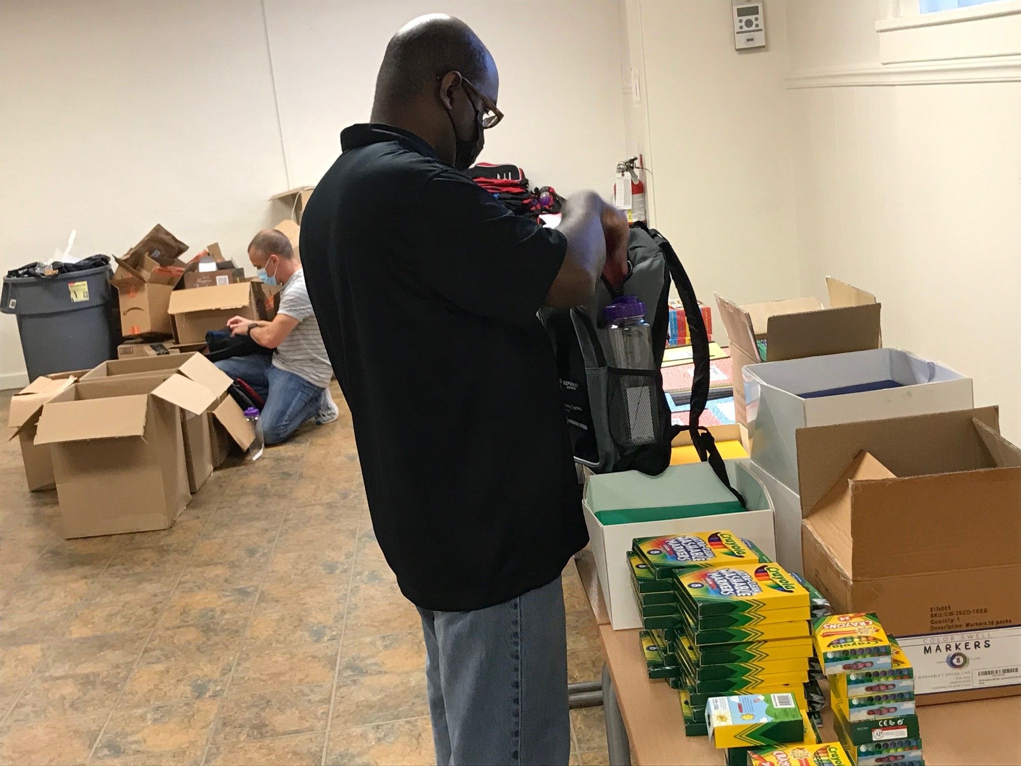 James Craig (front) and Christopher Policicchio stuff backpacks full of back-to-school supplies as part of DLC's volunteer partnership with Hosanna House.