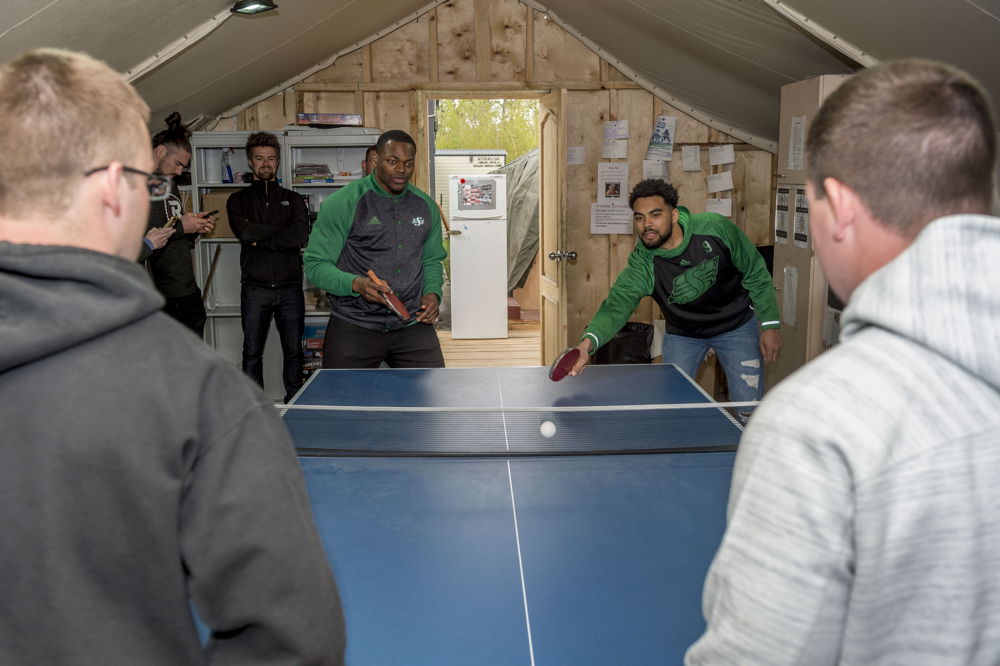 Henoc Muamba (G) and Nic Demski (D) jouent au tennis de table avec des militaires déployés dans le cadre de l'opération UNIFIER à Starychi, en Ukraine. Photo : CplC Mathieu Gaudreault, Caméra de combat des Forces canadiennes