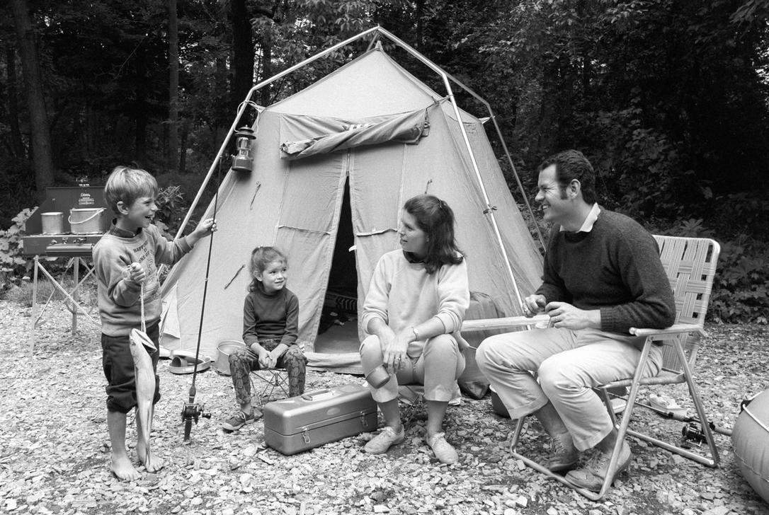 AKG2150247 1970s FAMILY OF FOUR SITTING IN FRONT OF TENT IN WOODS SON HOLDING FISHING POLE IN ONE HAND & BIG FISH IN OTHER.  © ClassicStock / akg-images / H. Armstrong Roberts